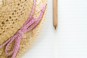 Closeup of a notebook, wooden pen and straw hat with a pink bow